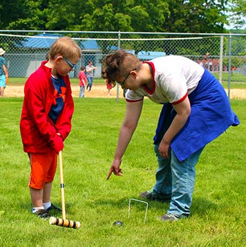 Two students at a special education school play croquet together during a picnic.