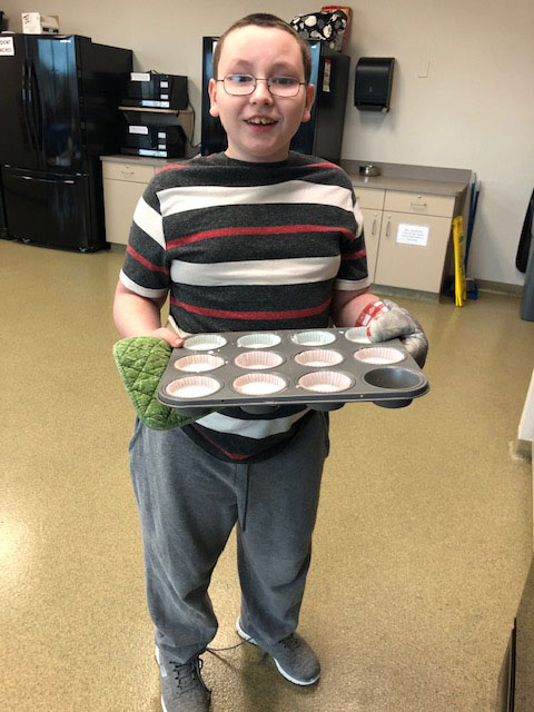 A special education student smiles for the camera and holds a tray of cupcakes