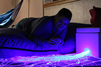 A high school student smiles at a string of lights in the sensory room of his special needs school
