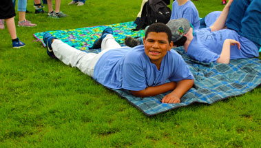 A high school student in a blue shirt smiles on a blanket.