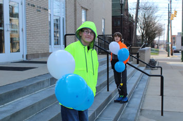 Two middle school boys hold baloons and smile on the steps of their special needs school.