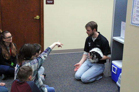 A man holds a black and white animal and talks to a group of special education students.