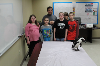 A group of special education students stand in front of a penguin and smile for the camera.