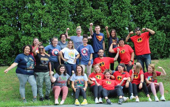 A group of special education teachers and staff smile in superhero shirts