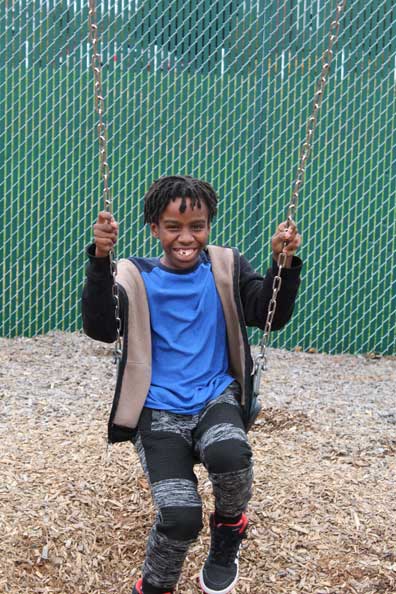 A special education student smiles from the swing on his school's playground