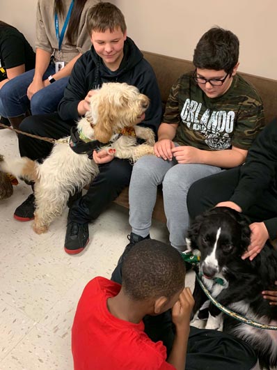 Two special education students pet a white dog during an event at their elementary school.