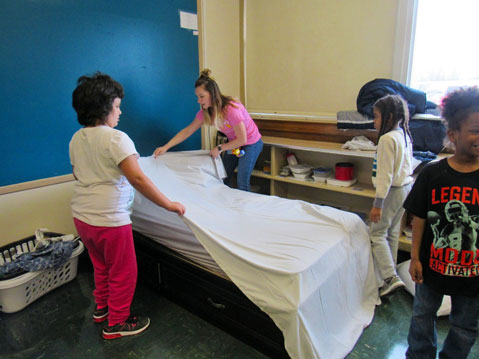 Three students in an autism support program work with their special education teacher on making a bed