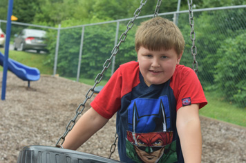 A special euducation student smiles at the camera while playing on a tire swing.